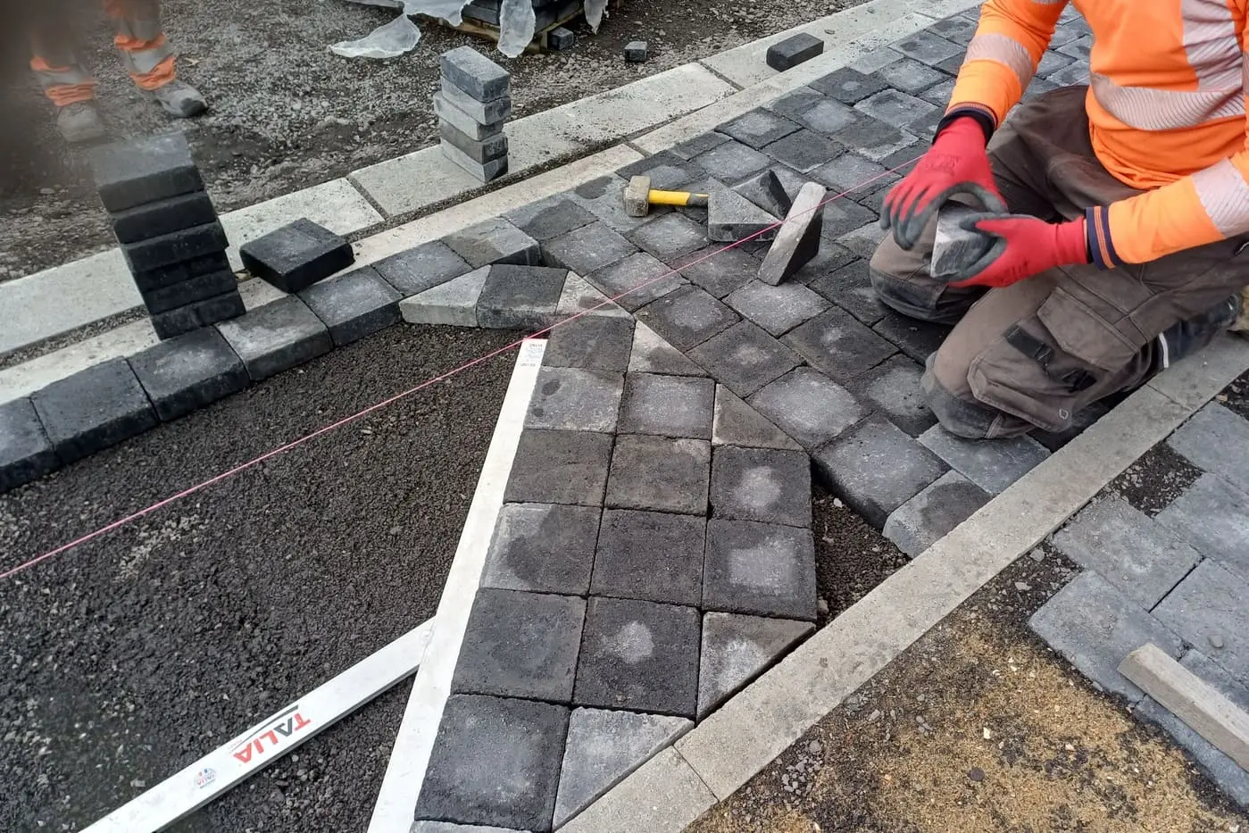 Apprenant posant des pavés en béton calibrés sur une chape lors d'une formation aux métiers des travaux publics.