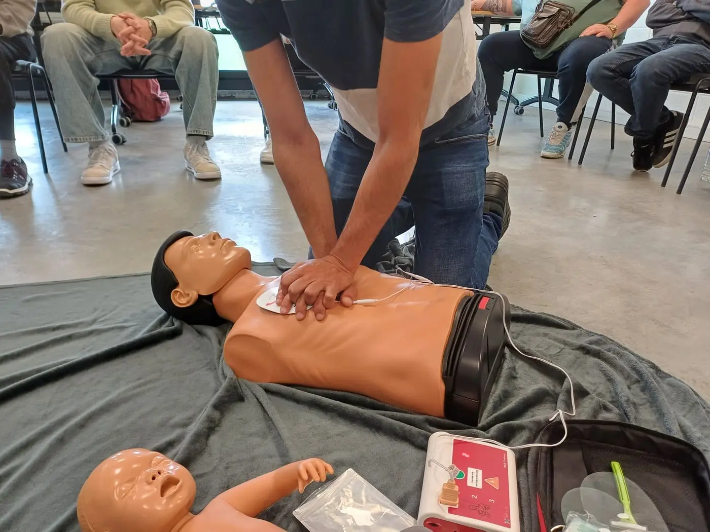 Apprenant pratiquant la réanimation cardio-pulmonaire et utilisant un défibrillateur lors d'une formation SST.